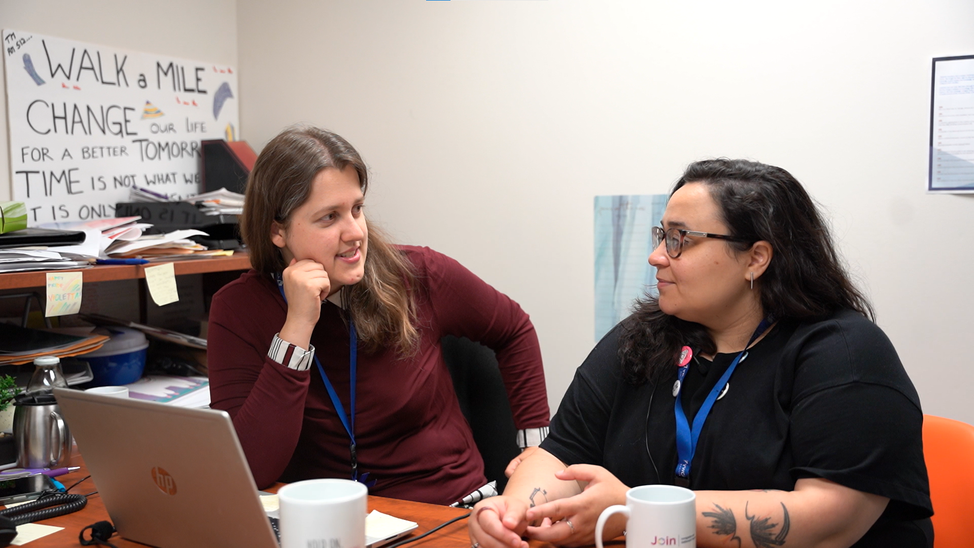 Two students sitting in front of a computer in an office talking