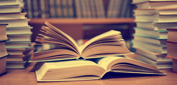 Two open books sitting in the middle of two separate stacks of books